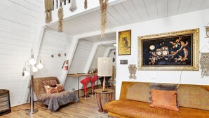Ein gemütliches Wohnzimmer im Loft-Stil mit hoher Decke, freiliegenden Holzbalken, einer Couch, einem Sessel und einem Couchtisch.