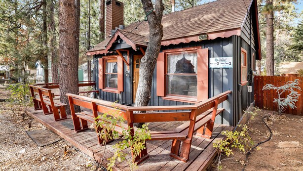 Un chalet rustique doté d’une terrasse en bois et de bancs, entouré de grands arbres.