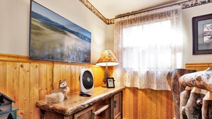 L'intérieur d'une cabane en bois, avec une commode en bois, une lampe, un ventilateur et un tableau encadré accroché au mur.