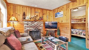 Un intérieur de chalet chaleureux avec une cheminée, un téléviseur, un canapé et un lit.