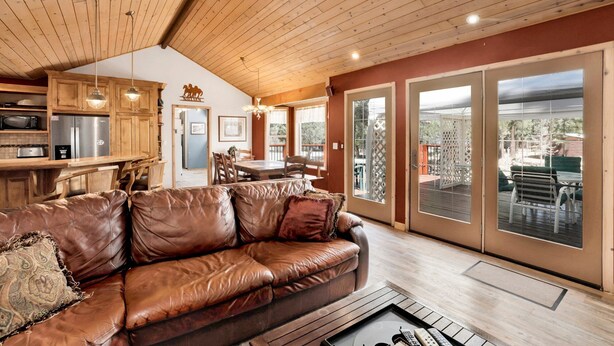 A spacious living area with a leather sofa, wooden ceiling, and a large sliding glass door leading to an outdoor patio. - ONE Hundred Pines Ranch #2005 (Big Bear City)