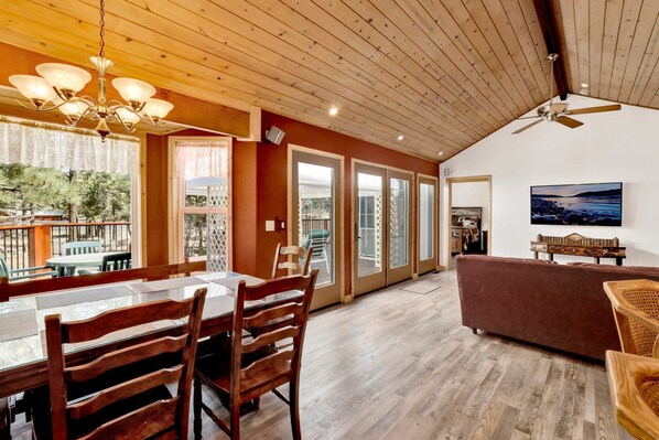 A spacious room with a wooden ceiling, a dining area with a table and chairs, a sofa, and a ceiling fan. - ONE Hundred Pines Ranch #2005 (Big Bear City)