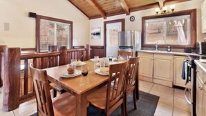 A wooden dining table with chairs, a refrigerator, a sink, and cabinets in a kitchen area. - Bear Tracks #2020 (Big Bear Lake)