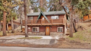 A two-story log cabin with a stone foundation, a balcony on the upper floor, and a front door with a window. - Bear Tracks #2020 (Big Bear Lake)