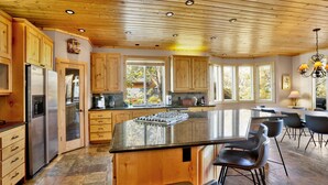 Una cocina amplia con armarios de madera, una isla grande con taburetes de bar y vistas al exterior a través de amplias ventanas.
