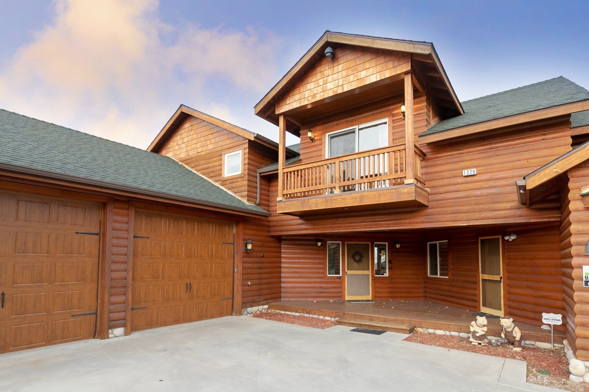 A two-story log cabin with a balcony, a garage, and a front door.