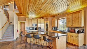 Una cocina moderna con armarios de madera, una isla central con taburetes de bar y suelo de baldosas de piedra.