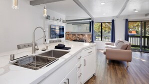 Una cucina moderna con una grande isola, piano cottura integrato e schienale in pietra. C'è un'area pranzo con un divano e un'ampia finestra che offre vista sull'esterno.