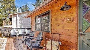 En stuga av trä med en veranda, nummer 280, med Adirondack-stolar och en hög med ved.