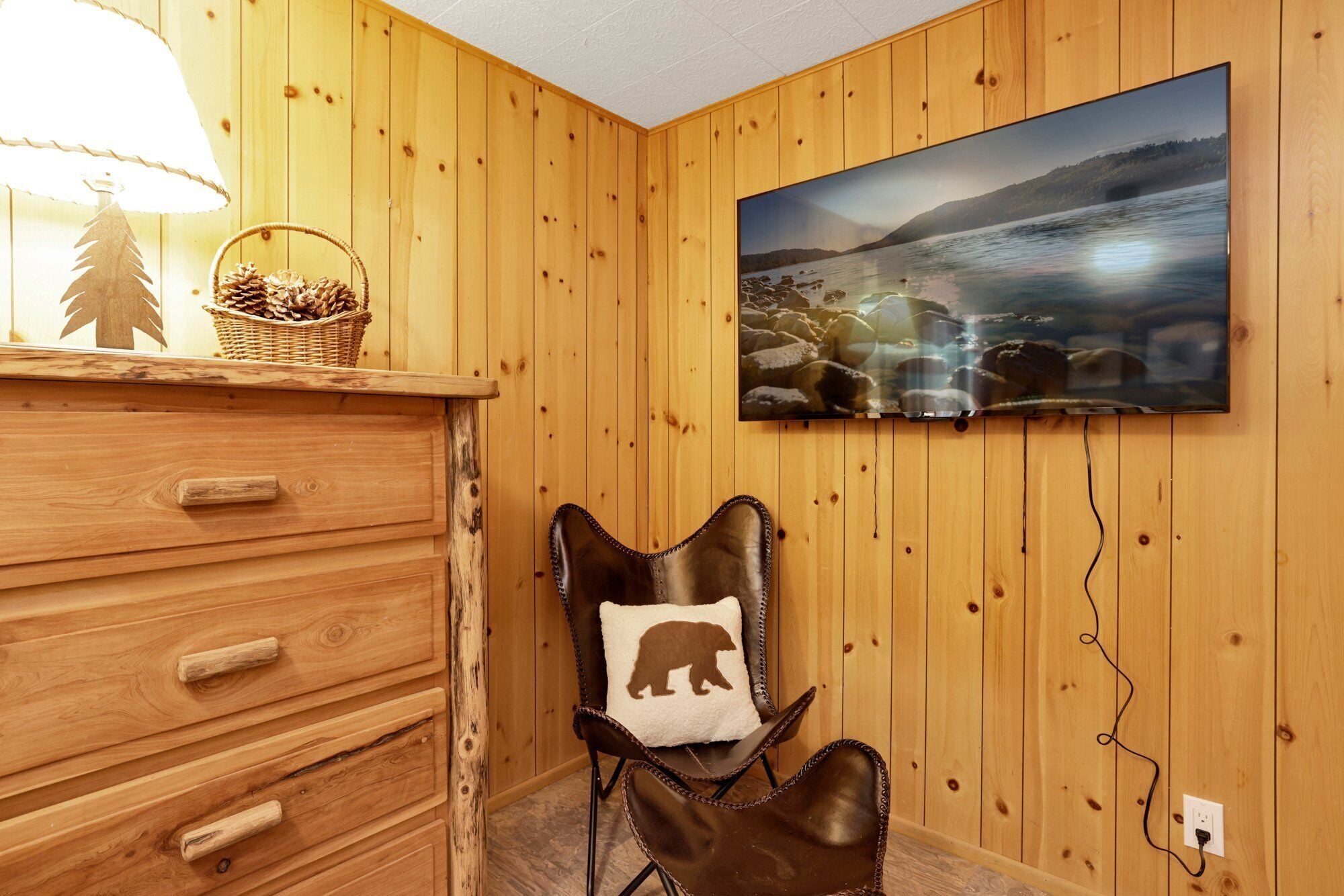Een kamer met houten lambrisering, een houten dressoir, een stoel met een kussen in de vorm van een beer en een groot landschap op de muur.