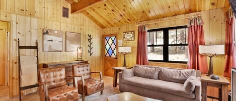 A cozy log cabin interior with a sofa, two leather chairs, a wooden coffee table, and a patterned rug.