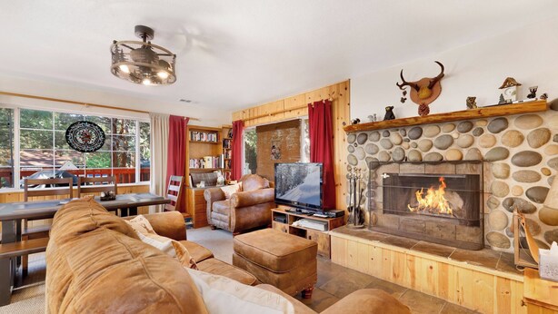A cozy living room with a stone fireplace, leather sofas, a television, and a bookshelf. - Montana Cabin #1938 (Big Bear City)