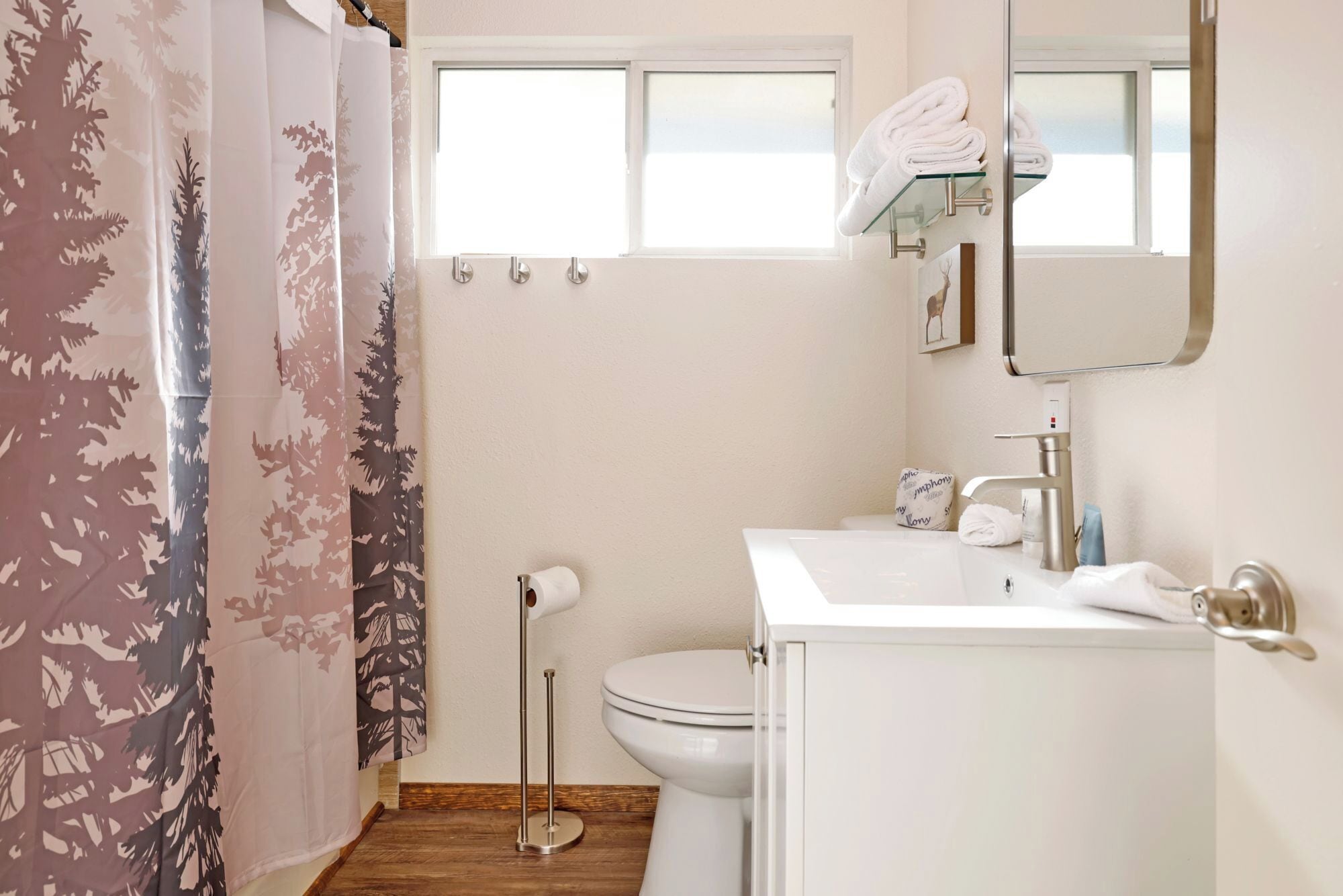 A bathroom with a toilet, sink, and mirror. There is a shower curtain with a tree pattern.