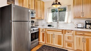 A kitchen with wooden cabinets, a stainless steel refrigerator, a stove, and a window with curtains. - Montana Cabin #1938 (Big Bear City)