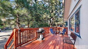 A wooden deck with a barbecue grill, two Adirondack chairs, and a bench. - Montana Cabin #1938 (Big Bear City)