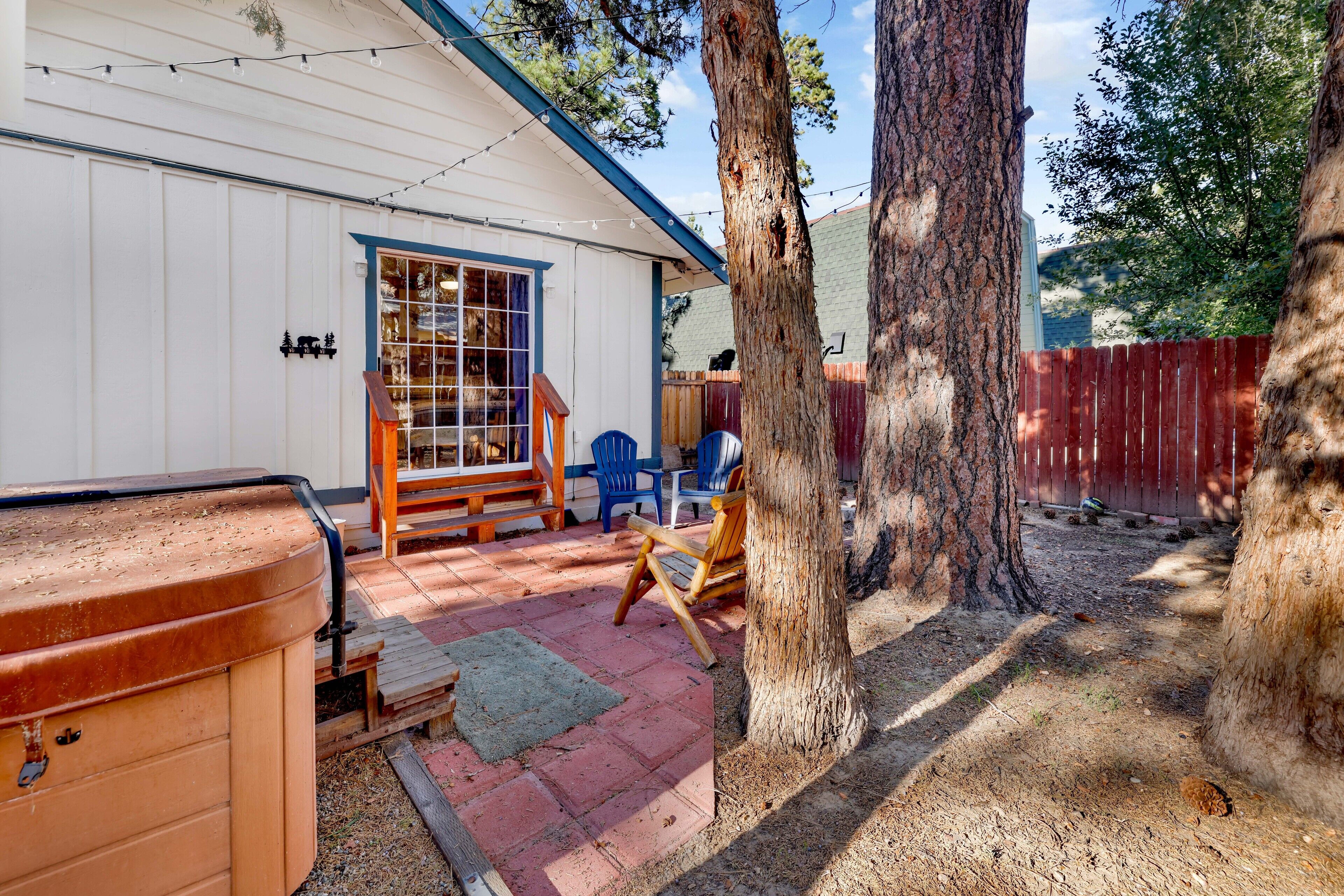A backyard with a wooden hot tub, a patio with blue chairs, and a wooden deck.