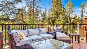 A deck with a wicker sofa, two side tables, and a glass coffee table. - Pine Meadow Village Castle #2301 (Big Bear Lake)