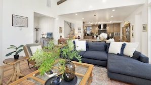 A spacious living room with a dark blue sofa, a wooden coffee table with a plant, and a staircase leading to a kitchen area. - Pine Meadow Village Castle #2301 (Big Bear Lake)