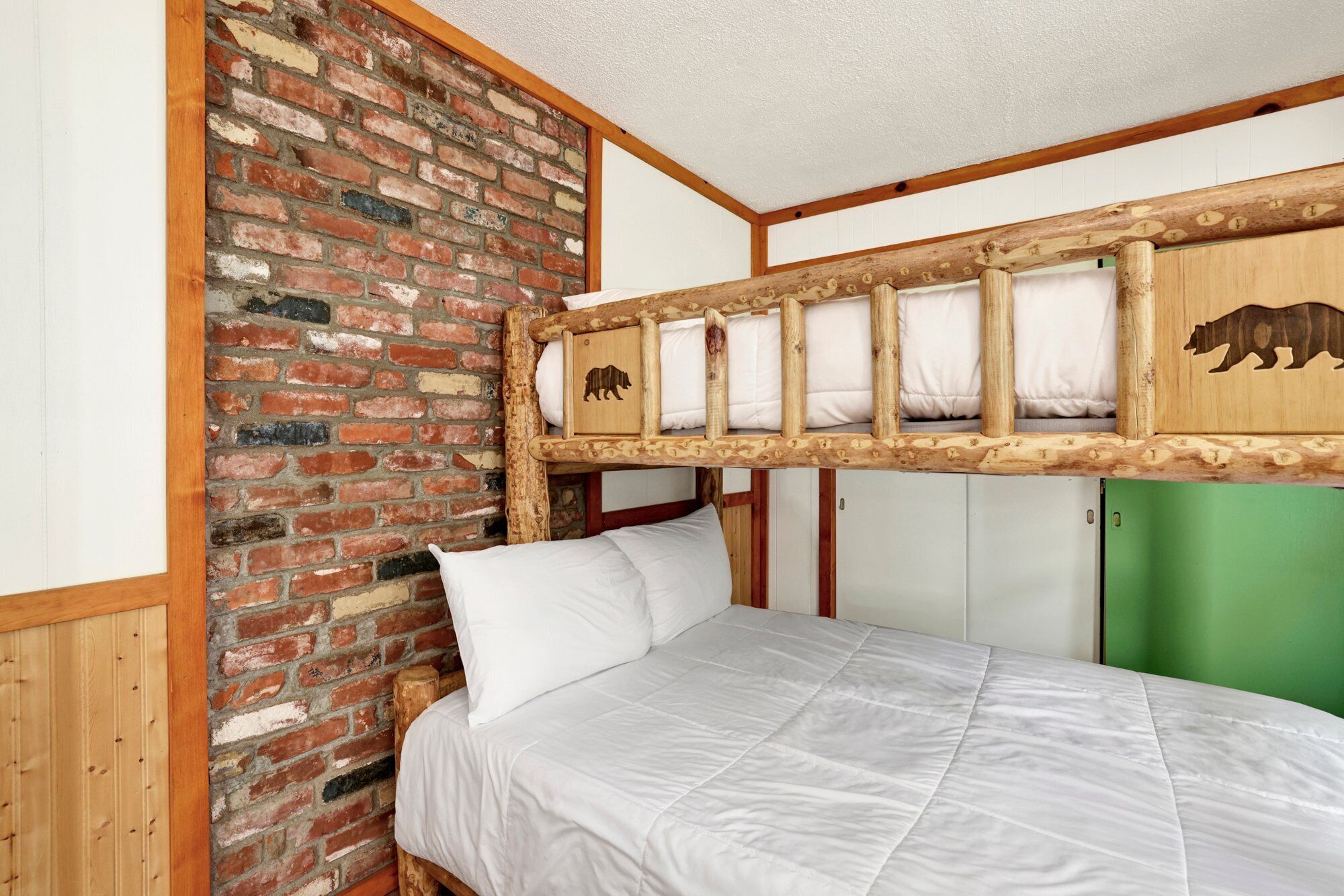 Un lit superposé avec une tête de lit en bois, un mur en briques et une porte verte.