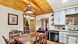 Uma sala de jantar com mesa e cadeiras de madeira, um candelabro e uma cozinha com armários e eletrodomésticos.