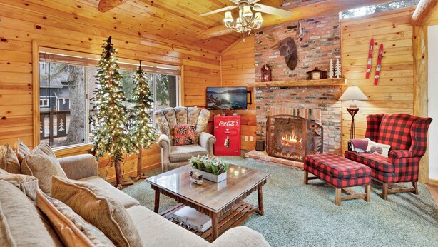 Interior acolhedor de uma cabana de madeira com lareira, uma janela grande, um pinheiro de Natal e uma televisão.