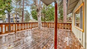 Um deck de madeira com guarda-corpo decorado com motivos de árvores, cercado por árvores altas.