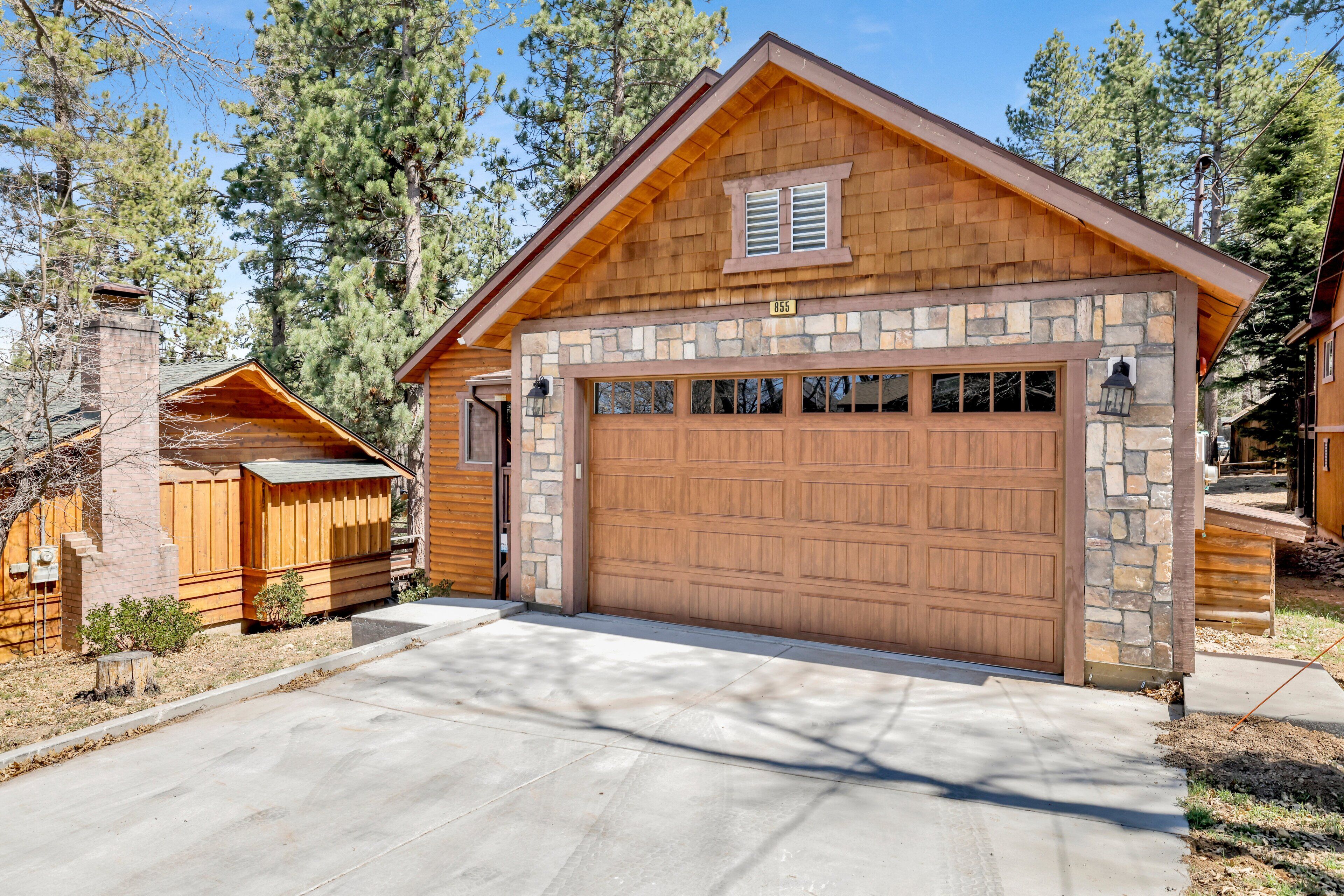 A wooden cabin with a stone foundation, a garage, and a chimney.