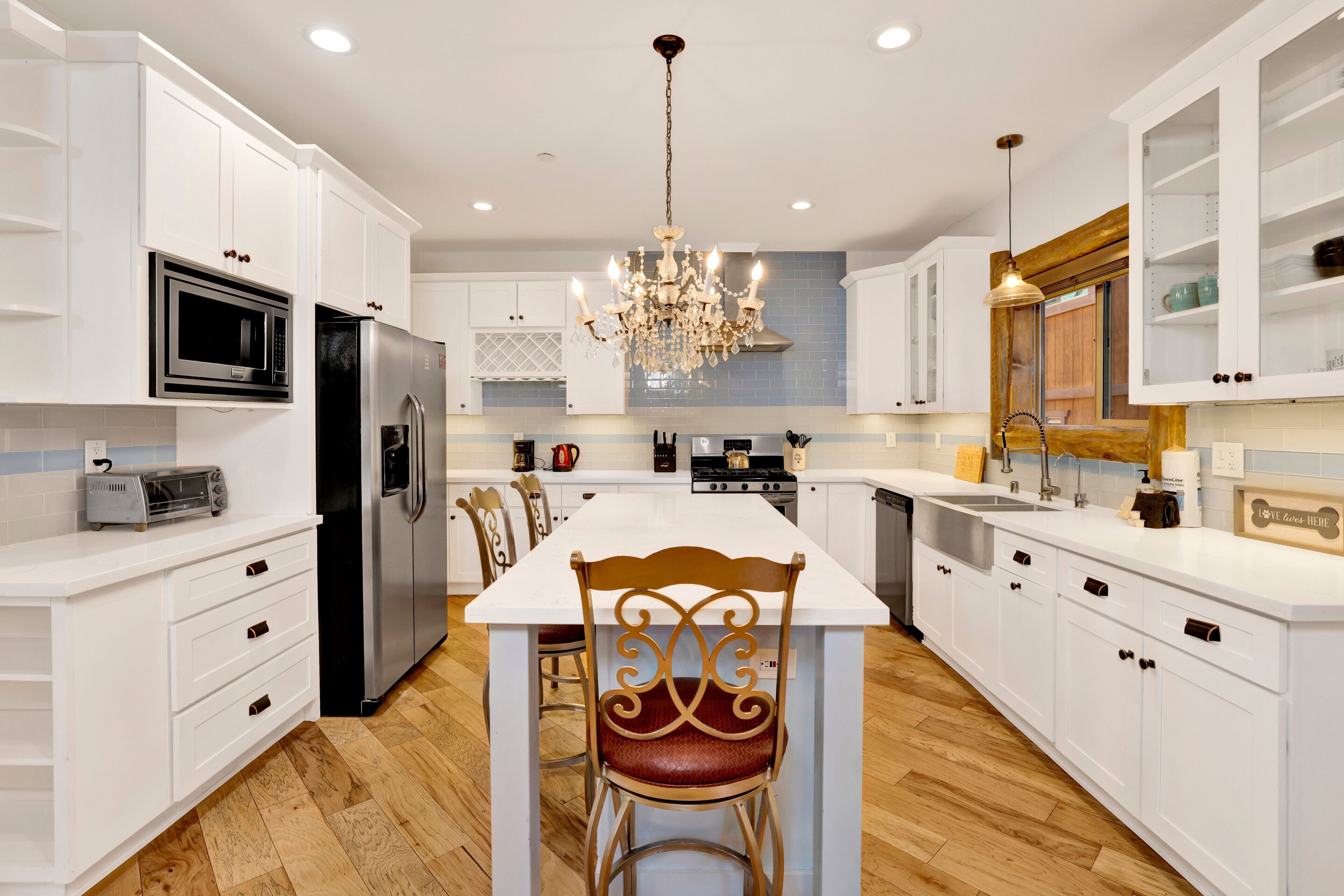 A modern kitchen with white cabinetry, a central island, a chandelier, and a dining area.