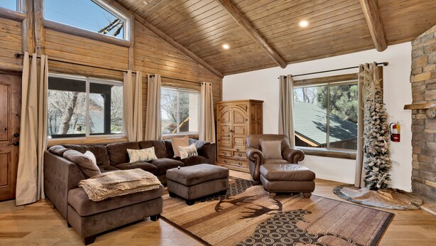 A spacious living room with a large window, wooden ceiling, and a fireplace. - Alpine Chalet #1840 (Big Bear Lake)