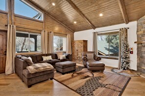A spacious living room with a large window, wooden ceiling, and a fireplace. - Alpine Chalet #1840 (Big Bear Lake)