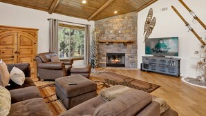 A cozy living room with a stone fireplace, leather sofas, and a television. - Alpine Chalet #1840 (Big Bear Lake)