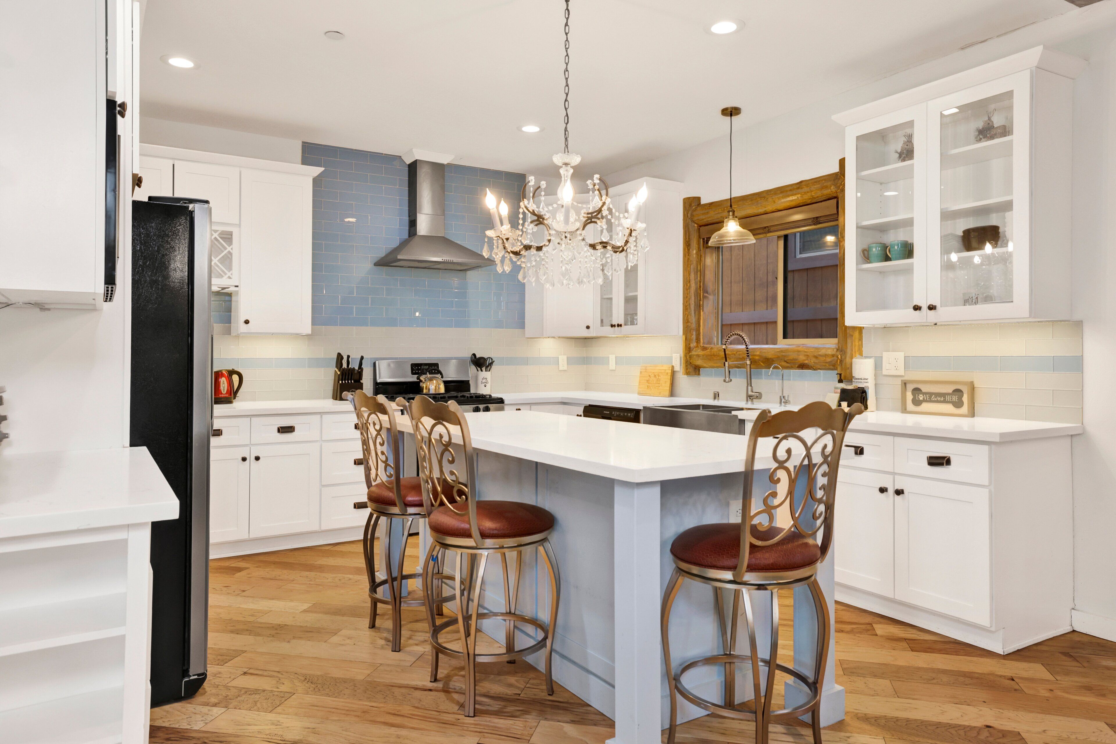 A kitchen with white cabinets, a central island with bar stools, a chandelier, and a large mirror above the sink.