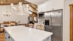 A modern kitchen with a large island, stainless steel appliances, and a chandelier. - Alpine Chalet #1840 (Big Bear Lake)