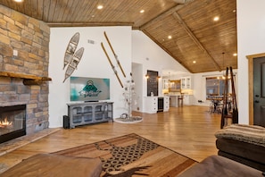 A spacious living area with a fireplace, wooden ceiling, and a television mounted on the wall. - Alpine Chalet #1840 (Big Bear Lake)