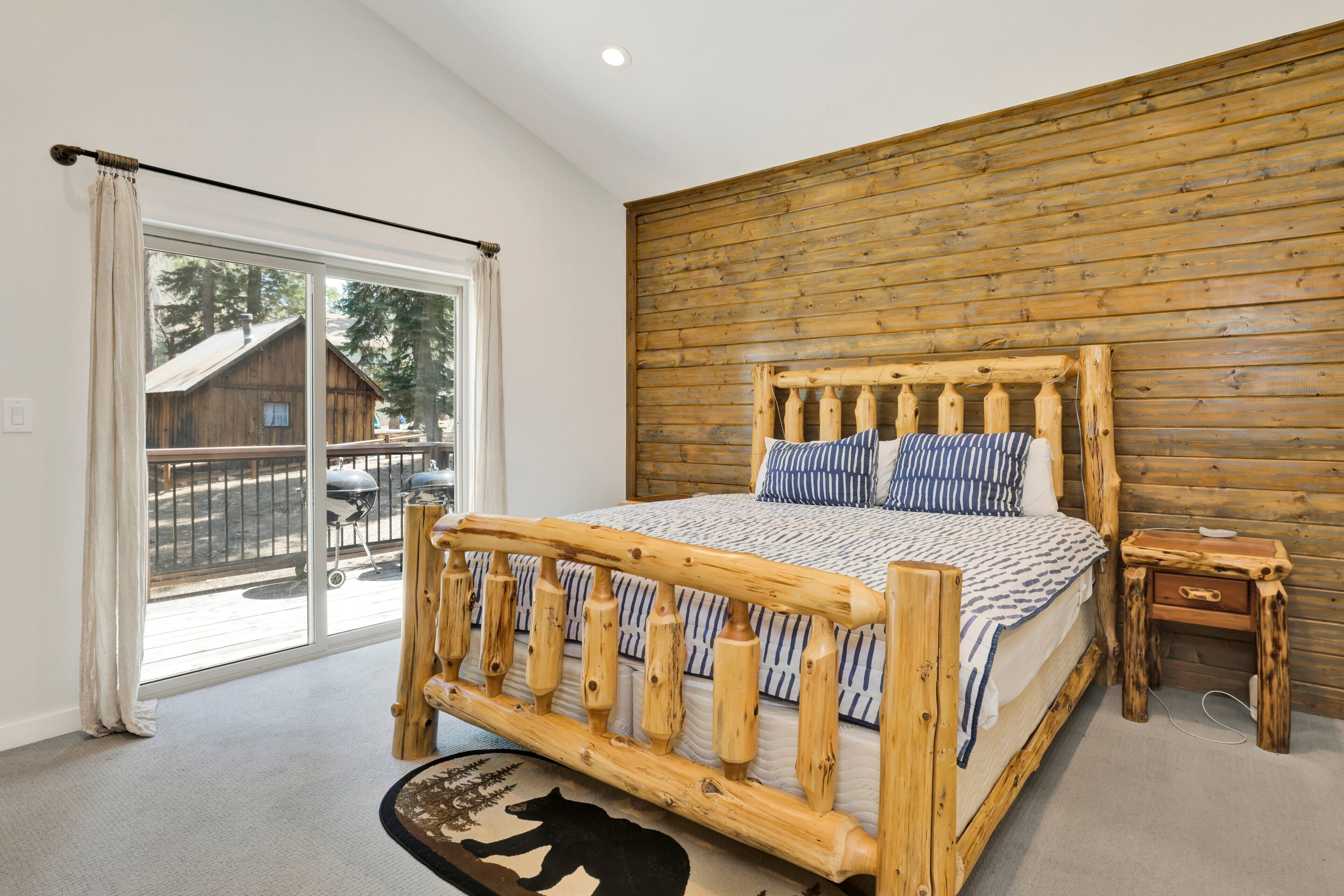 A bedroom with a wooden bed frame, a window with curtains, and a view of the outside.