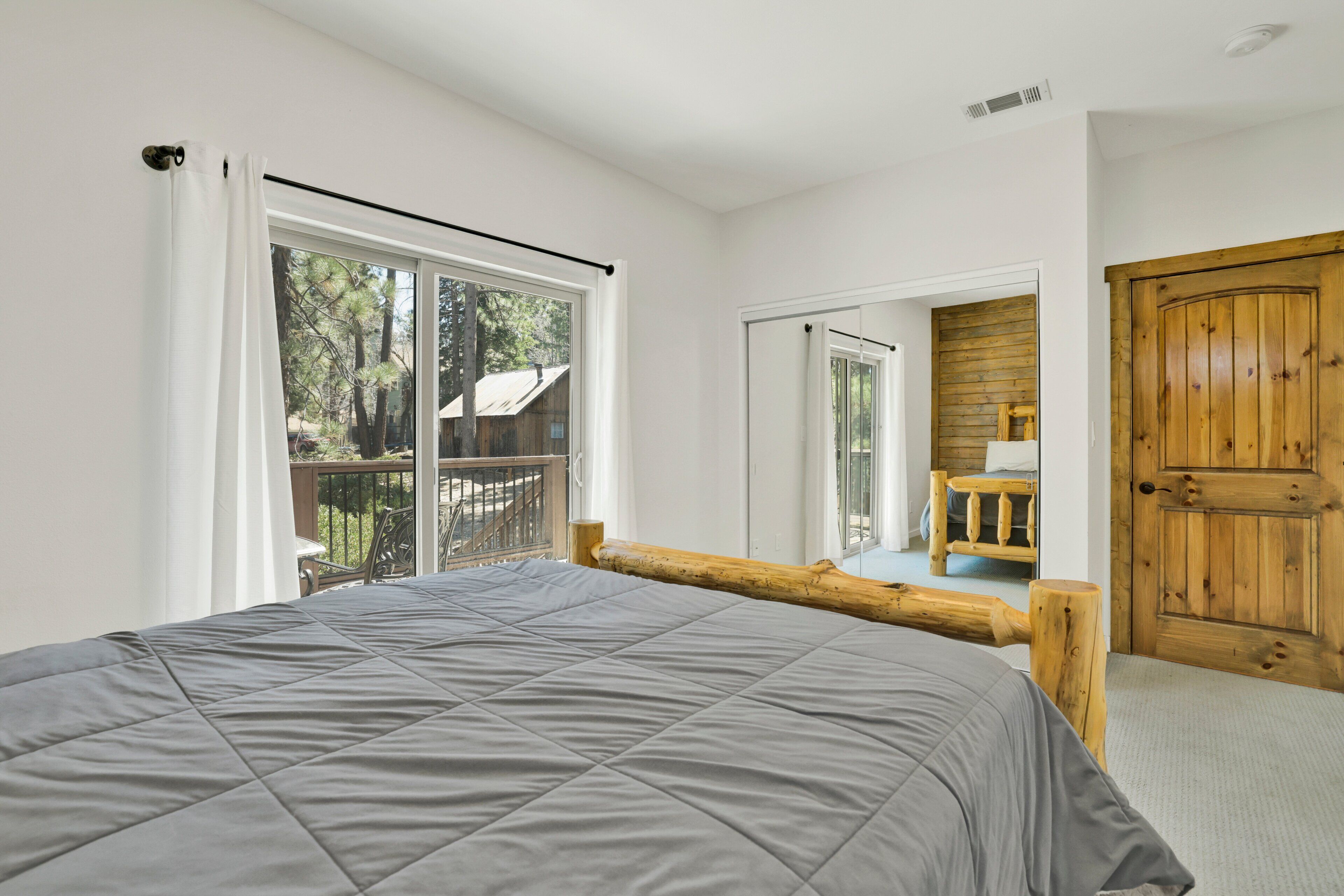 A bedroom with a large bed, a wooden door, and a balcony with a view of trees.