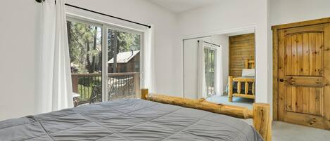 A bedroom with a large bed, a wooden door, and a balcony with a view of trees.