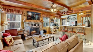 Una sala de estar acogedora con chimenea de piedra, televisor y una zona de bar con taburetes.