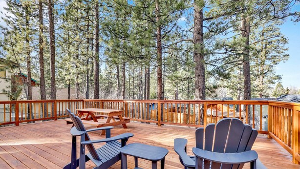 Una terraza al aire libre con barandillas de madera, una mesa de picnic y sillas Adirondack.