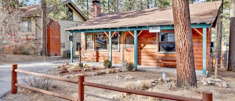 A rustic log cabin with a porch, a chimney, and a small garden area.