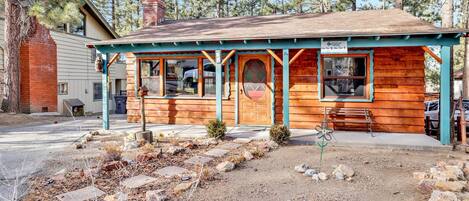 A rustic wooden cabin with a porch, a chimney, and a 'No Street Parking' sign.