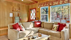 Interior acogedor de una cabaña con detalles de madera, un ventanal con vistas al exterior y un sofá modular con cojines rojos.