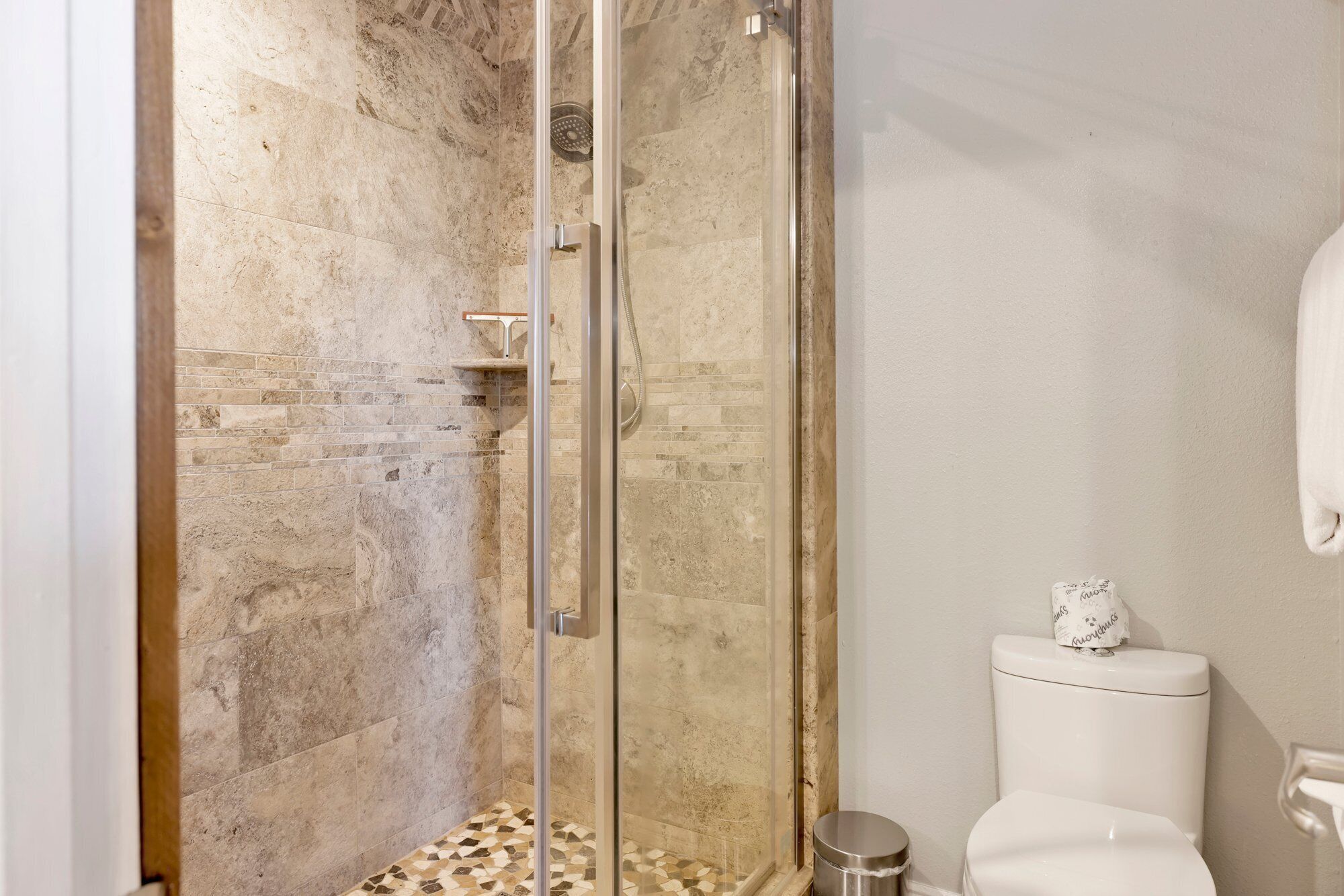 A bathroom with a glass-enclosed shower, a tiled floor, and a white toilet.