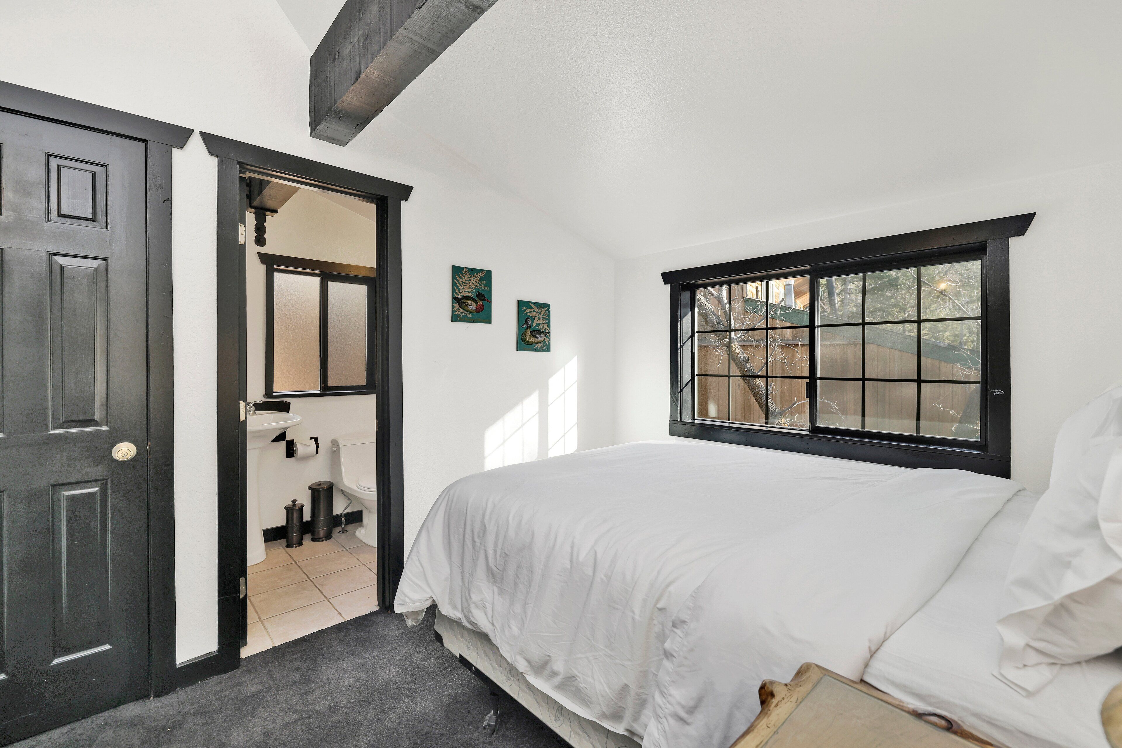 A bedroom with a bed, a window, a door, and a bathroom visible through an open door.