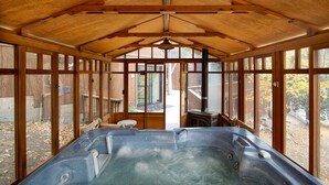 Ein Whirlpool in einer Holzhütte mit großen Fenstern, einem Deckenventilator und Blick ins Freie.