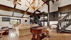 Ein geräumiges Wohnzimmer mit Holzboden, einem Kicker, einer Couch und einer Holztreppe.