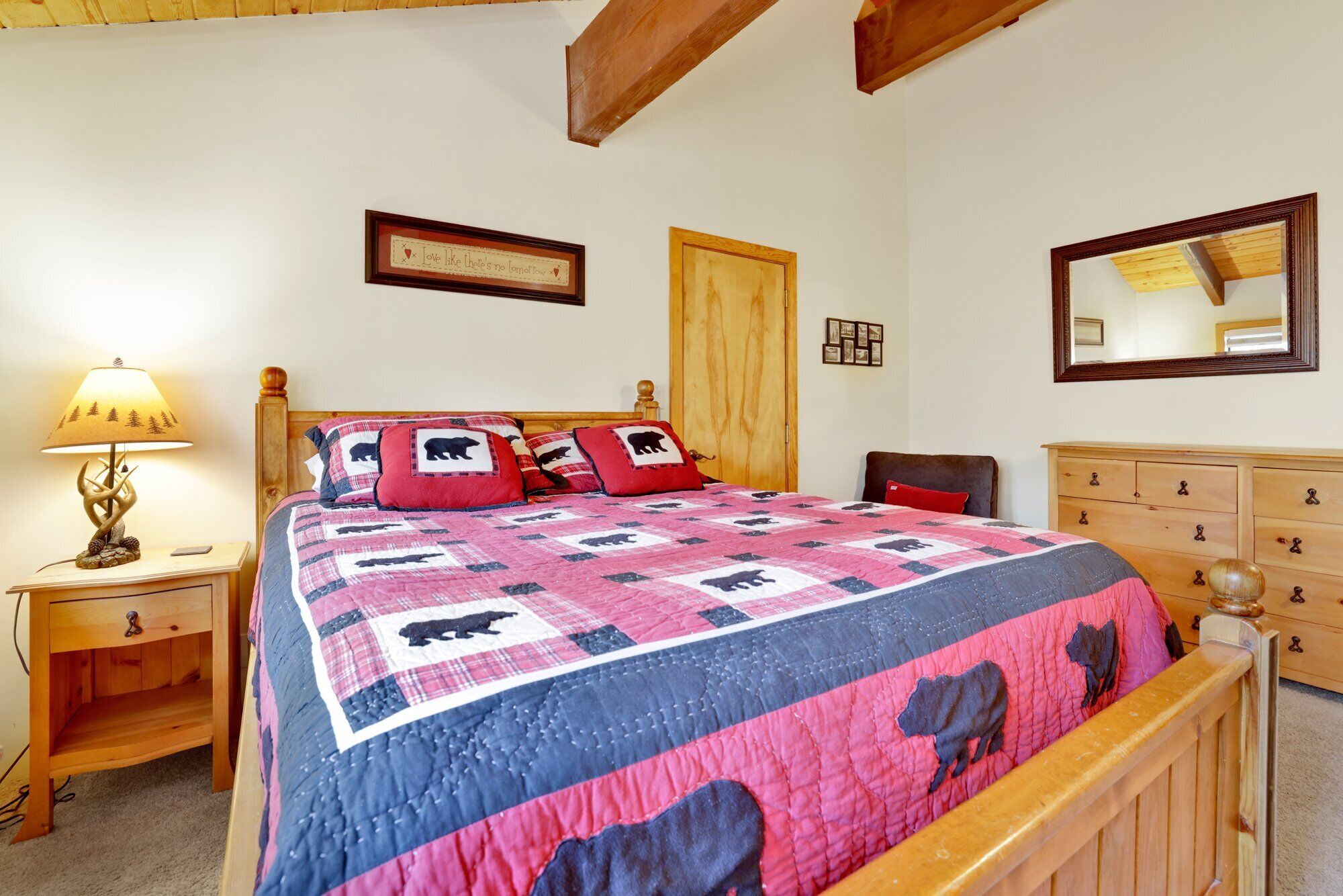 Un dormitorio con una cama de madera, una mesita de noche con lámpara, un aparador y un espejo en la pared.