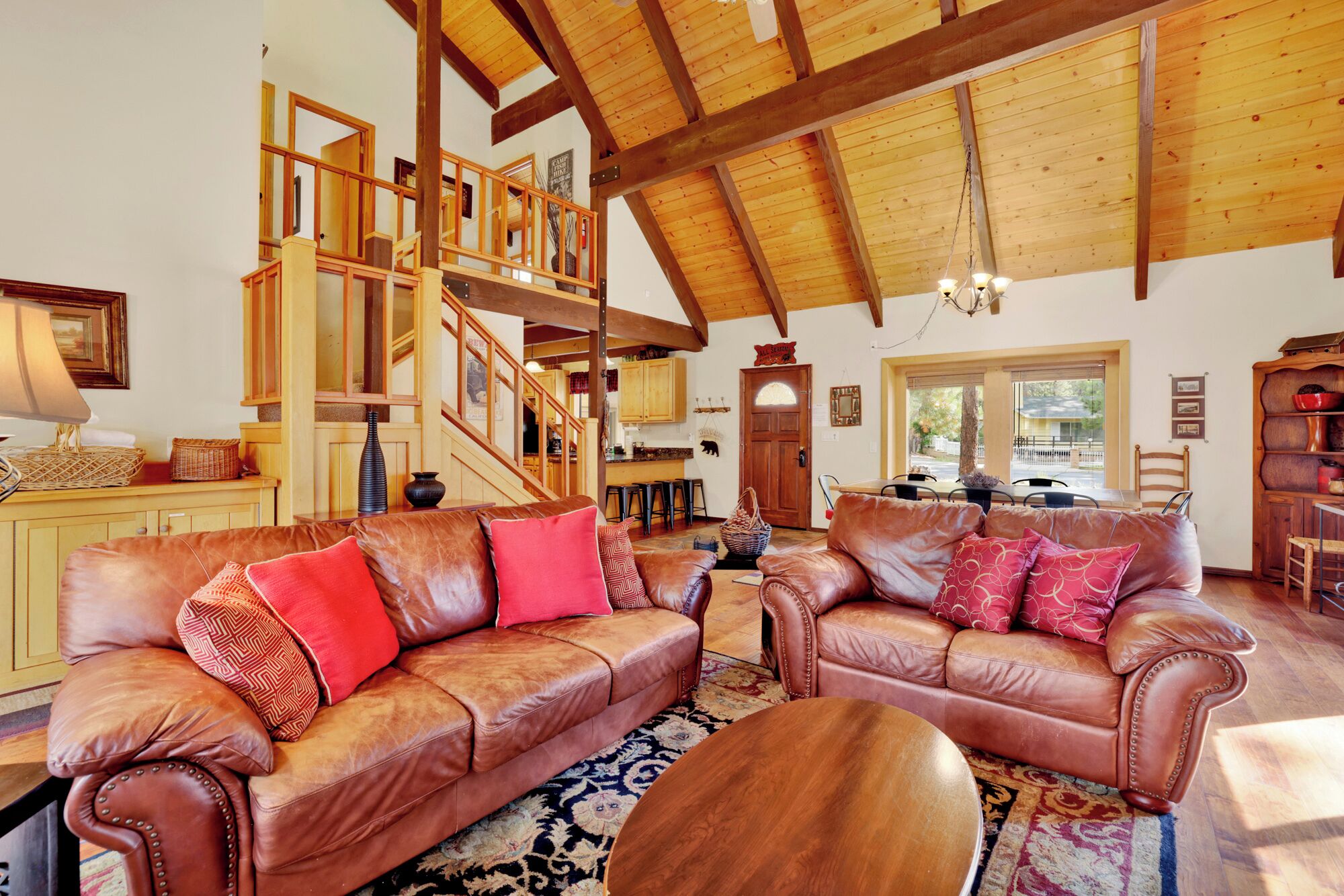 A spacious living area with leather sofas, a wooden staircase, and a kitchen in the background.
