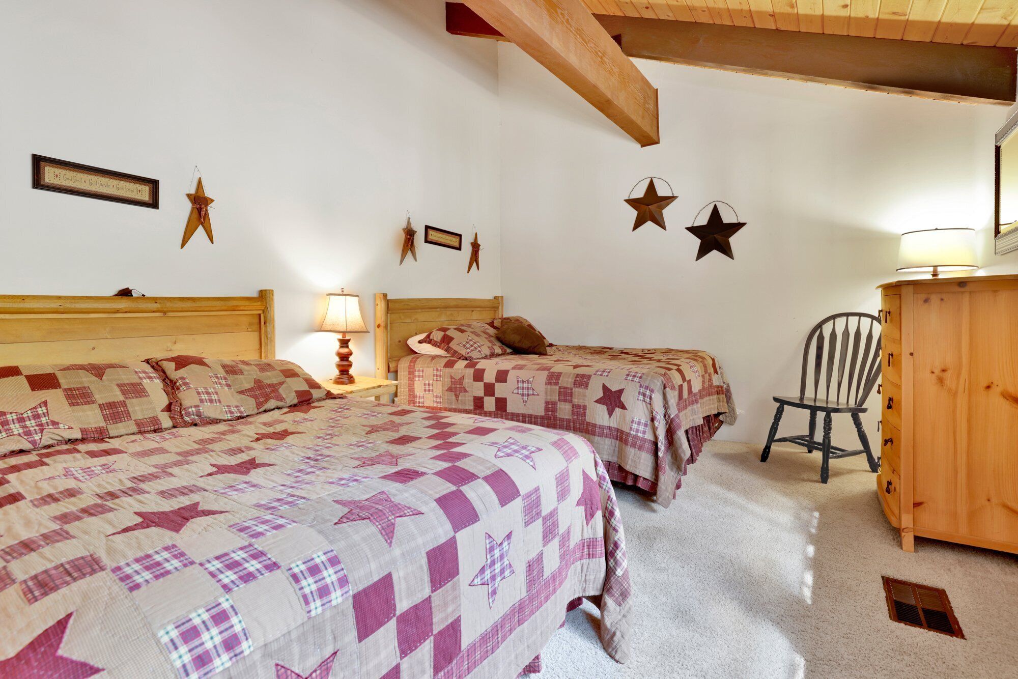 A cozy bedroom with two beds, a wooden dresser, and decorative stars on the wall.