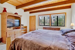 A bedroom with a large bed, wooden furniture, a television, and a window with a view of trees.